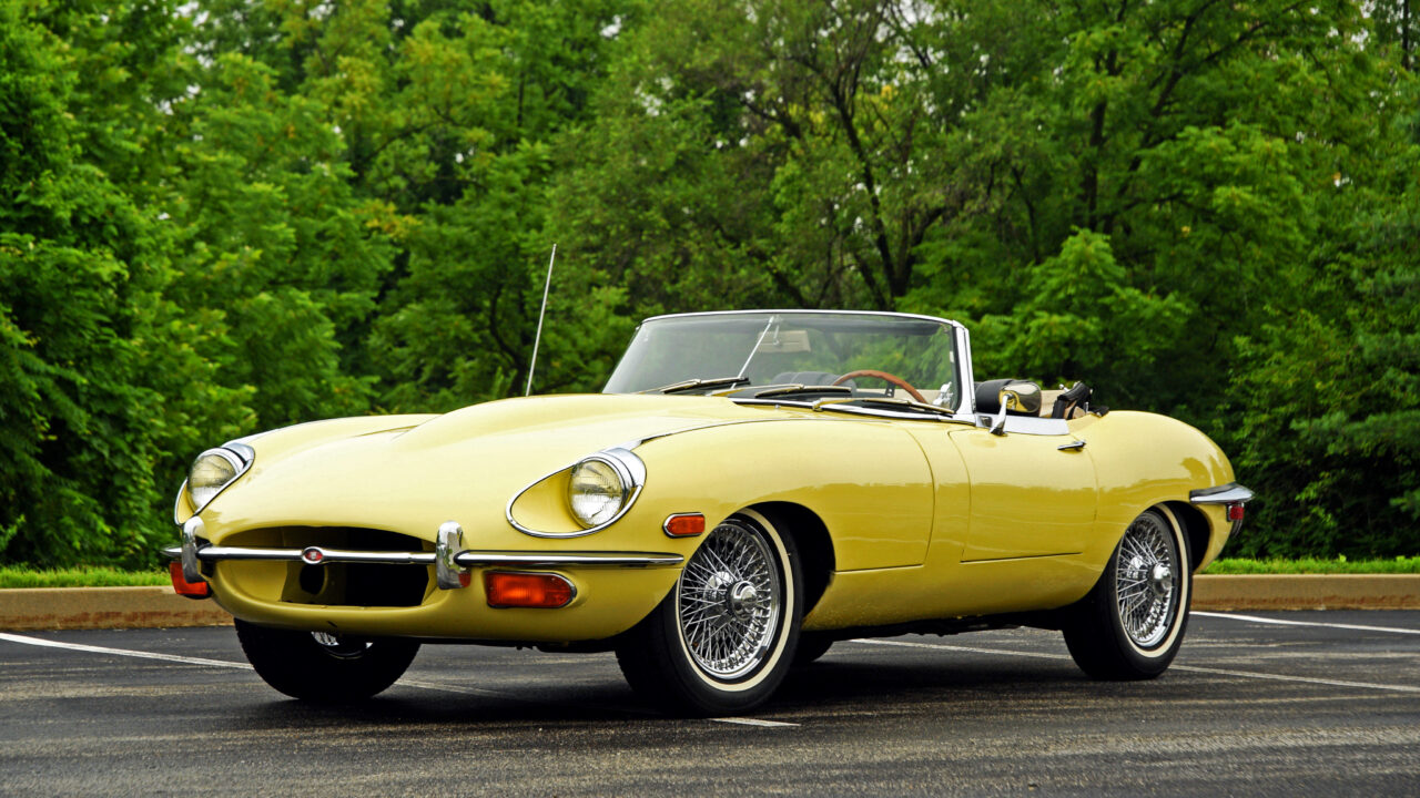 Stunning Yellow 1968 Jaguar E-Type Convertible Against Green Backdrop Wallpaper