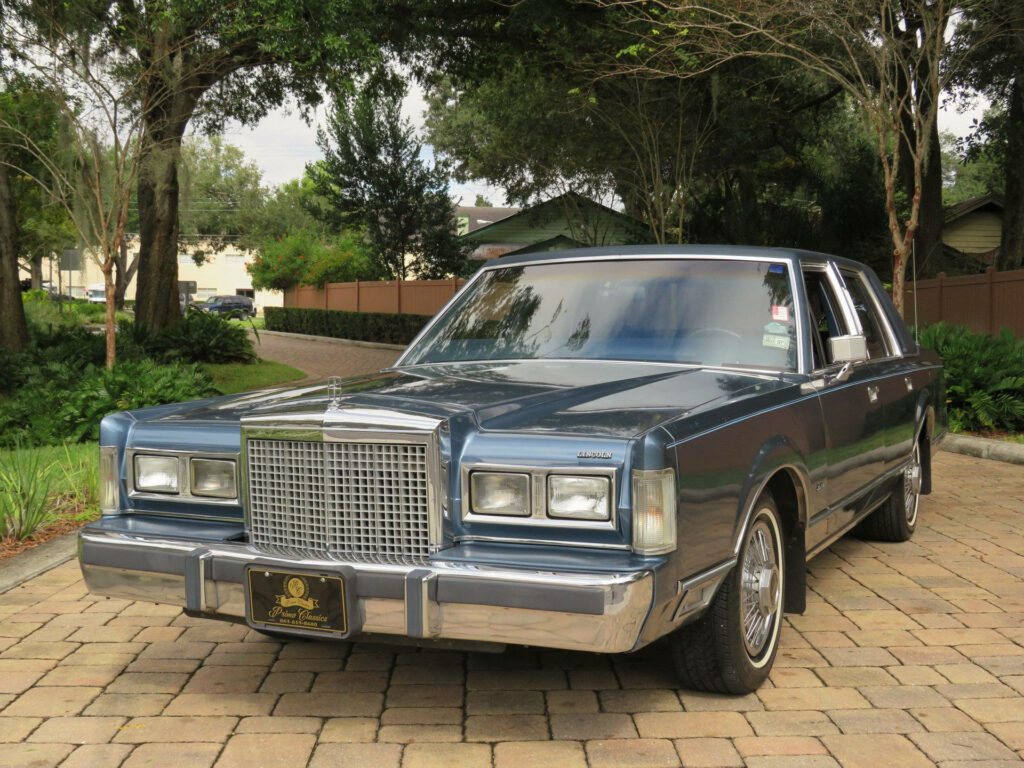 1986 Lincoln Town Car parked on driveway with polished chrome and lush green trees background Wallpaper