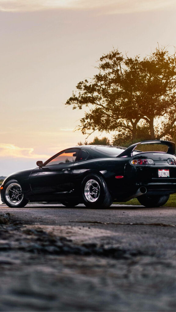 Black 1996 Toyota Supra Mk4 rear view with large spoiler and rims at sunset scenic roadside background Wallpaper