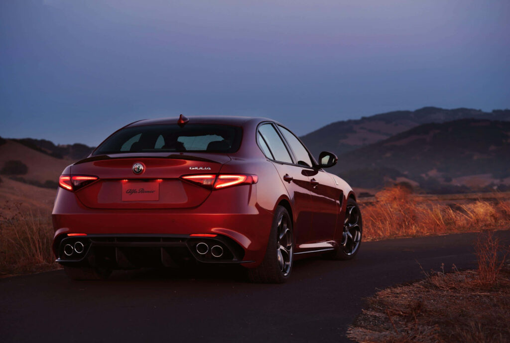 Red 2018 Alfa Romeo Giulia parked on scenic hill road with serene evening sky background wallpaper