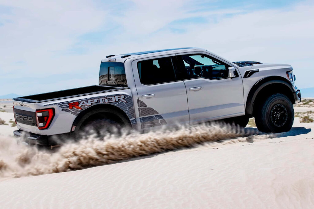 2023 Ford F-150 Raptor Supercrew Cab off-road driving on desert sand with clear blue sky background Wallpaper