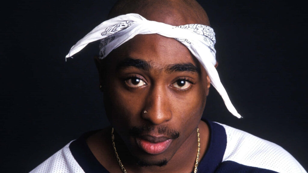 All Eyes on 2Pac: Legendary Rapper Poses with Iconic White Bandana in Striking Background Shot Wallpaper