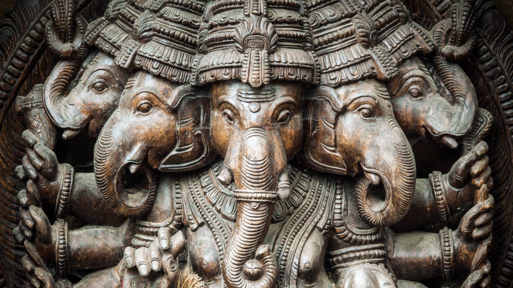 3D carved wooden Lord Ganesh statue wallpaper with intricate dark wood details and soft lighting