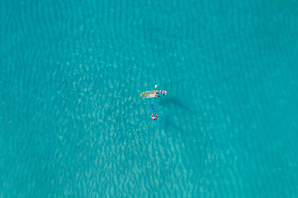 4K drone view of small boat and paddleboard on clear turquoise water vibrant wallpaper background