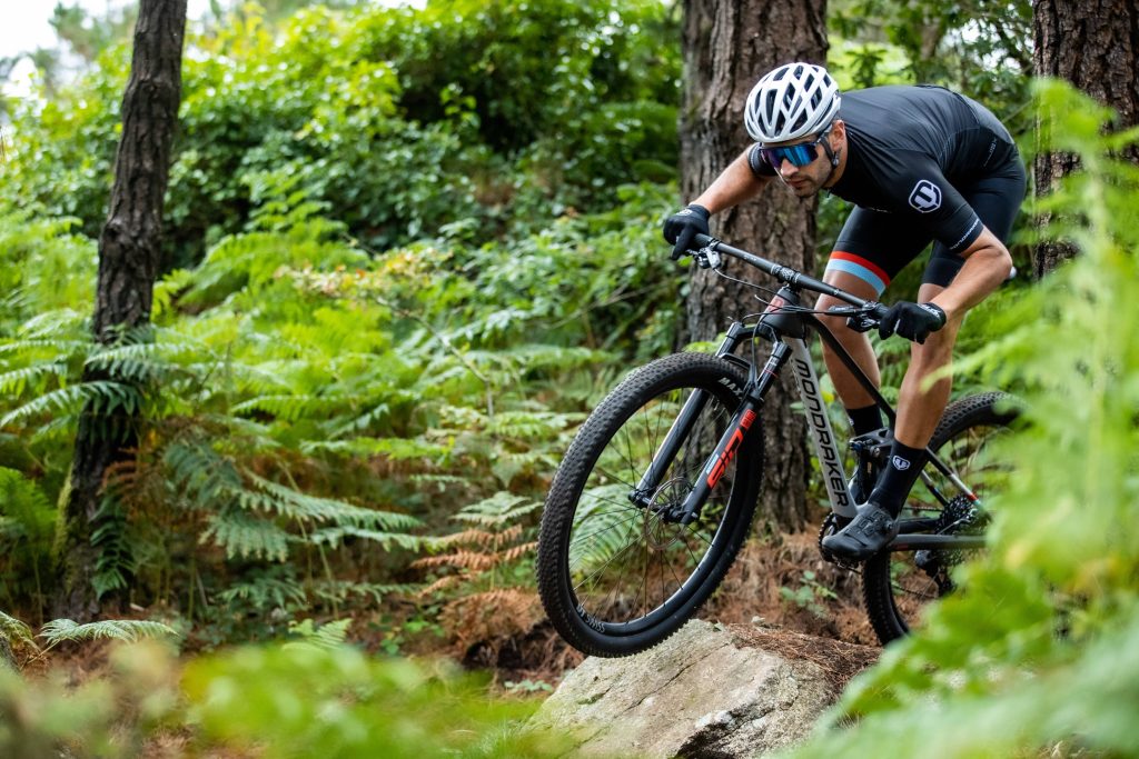 Cyclist rides Mondraker mountain bike on rocky forest trail surrounded by green ferns 4k wallpaper