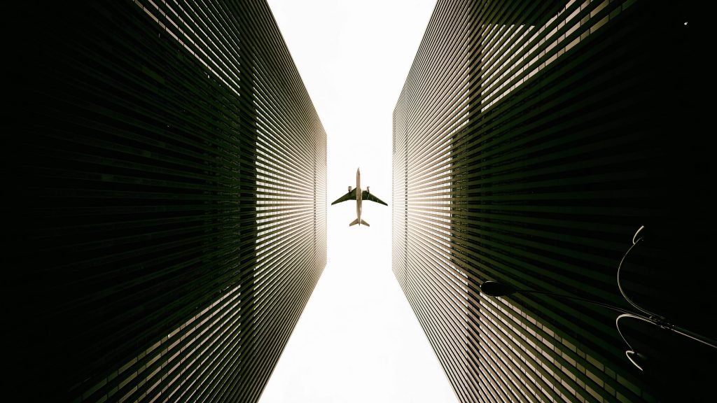 Commercial jet flying between two tall symmetrical skyscrapers in dramatic low-angle urban scene Wallpaper