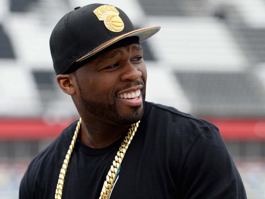 50 Cent smiling onstage wearing black cap gold chain iconic rapper style dynamic wallpaper
