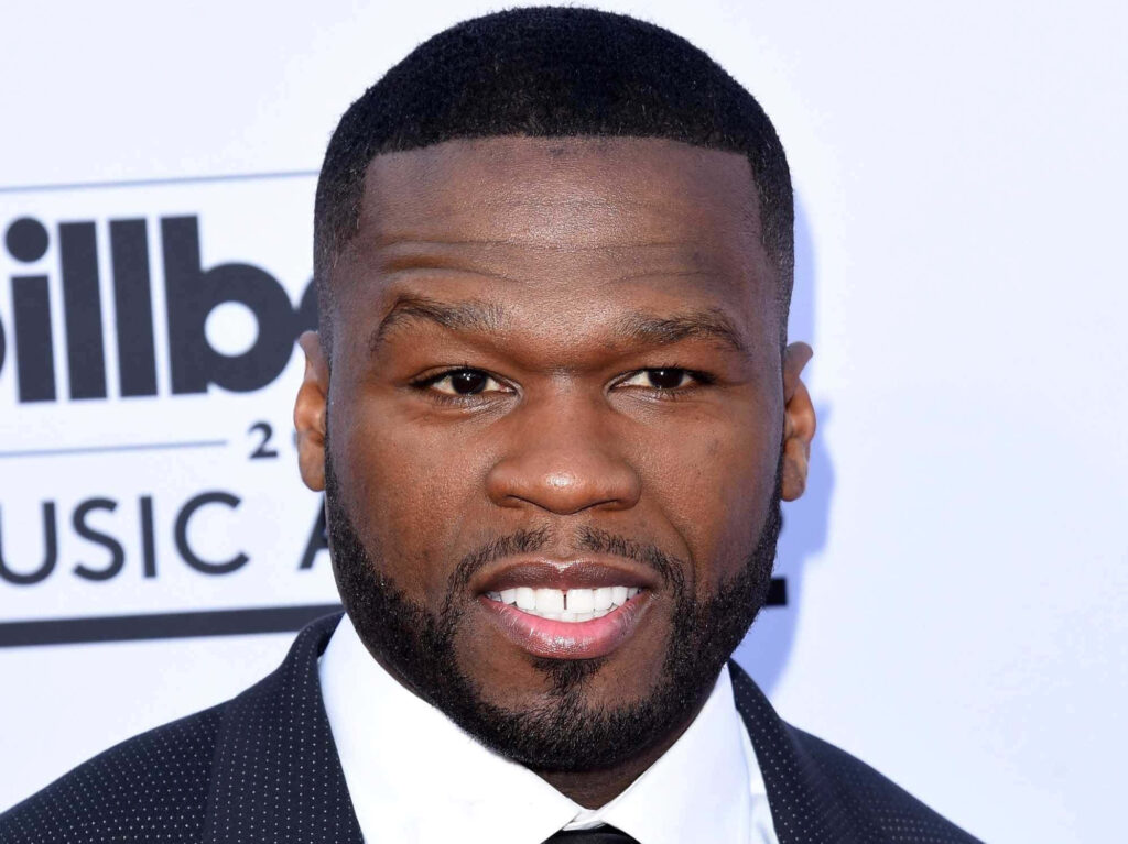 50 Cent in suit smiling confidently on red carpet showcasing charisma and bold personality wallpaper