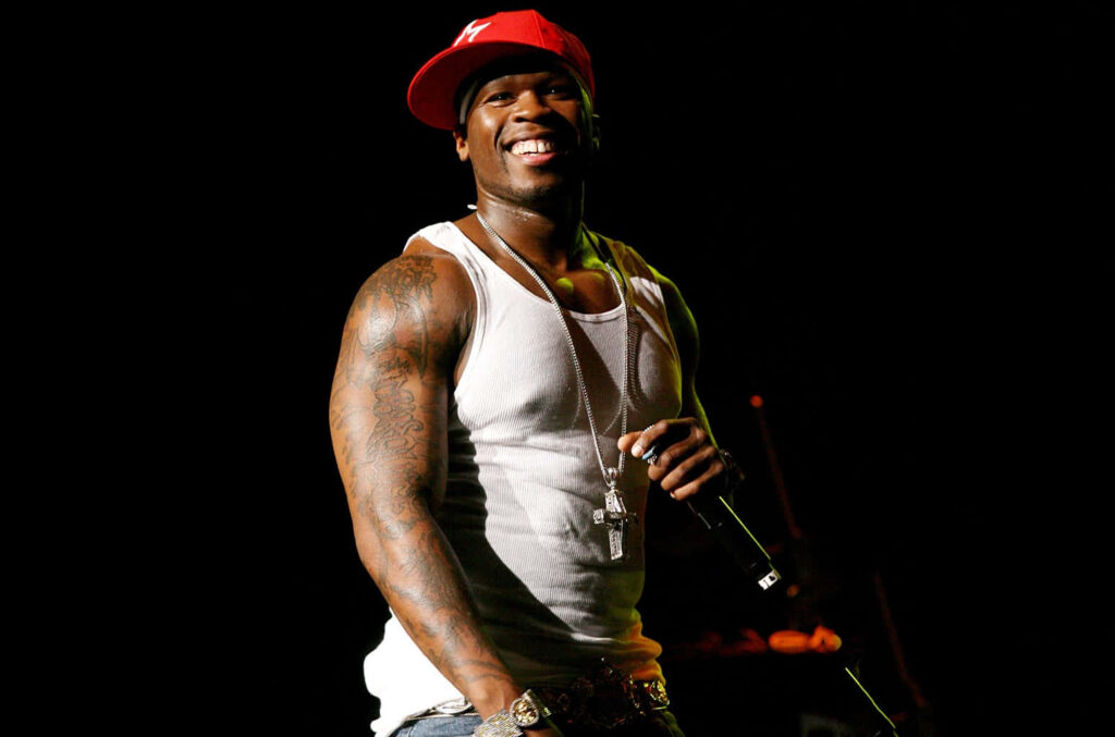 50 Cent on stage wearing white tank top and red cap exuding energy and charisma wallpaper