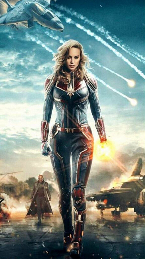 Heroic Duo Defends in the Chaos: Marvelous Captain Marvel iPhone Wallpaper Showcases Brie Larson alongside Nick Fury amidst Fighter Jets in an Astonishing Warzone