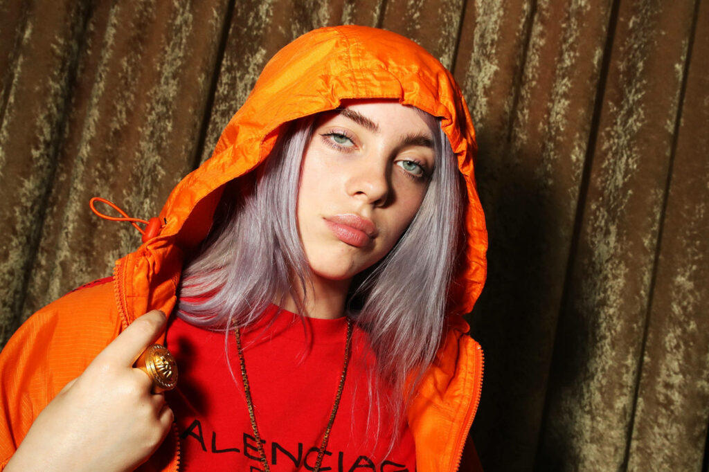 Gorgeous Billie Eilish donning an Orange Balenciaga Shirt, posing against a rustic wooden backdrop - Stunning 4k Billie Eilish background snapshot Wallpaper