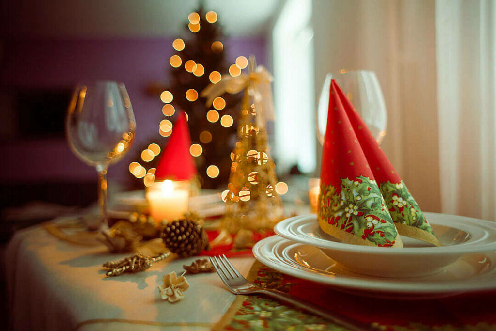 A Festive Holiday Table Setting with a Red Napkin, Candle, Wine Glass, and White Plate amidst a Beautifully Blurred Christmas Tree Background Wallpaper