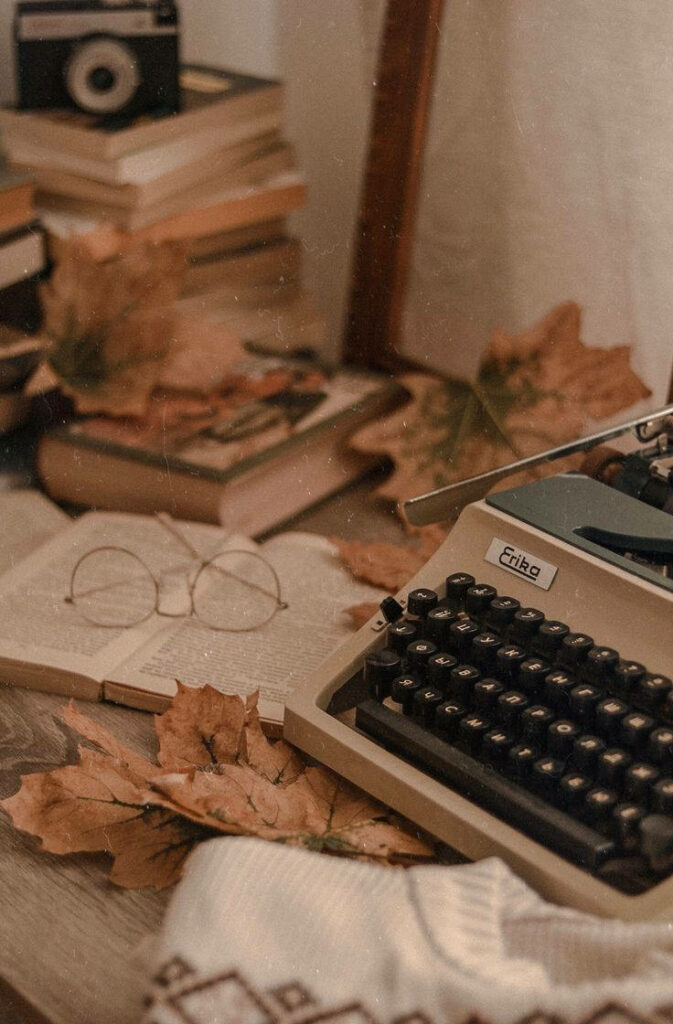 Vintage Vibes: Autumn Leaves, Typewriter, and Books on a Rustic Table Wallpaper