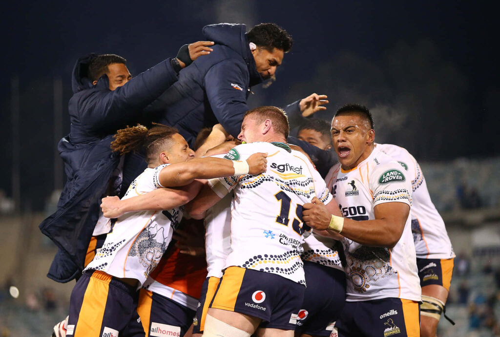 ACT Brumbies rugby players celebrating intense moment in white blue gold jerseys stadium lighting Wallpaper