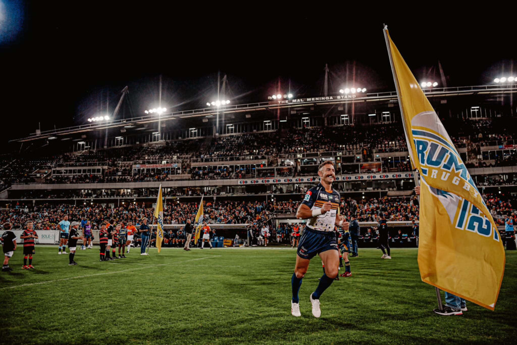 ACT Brumbies rugby player running with flag on green field at night GIO Stadium live match wallpaper