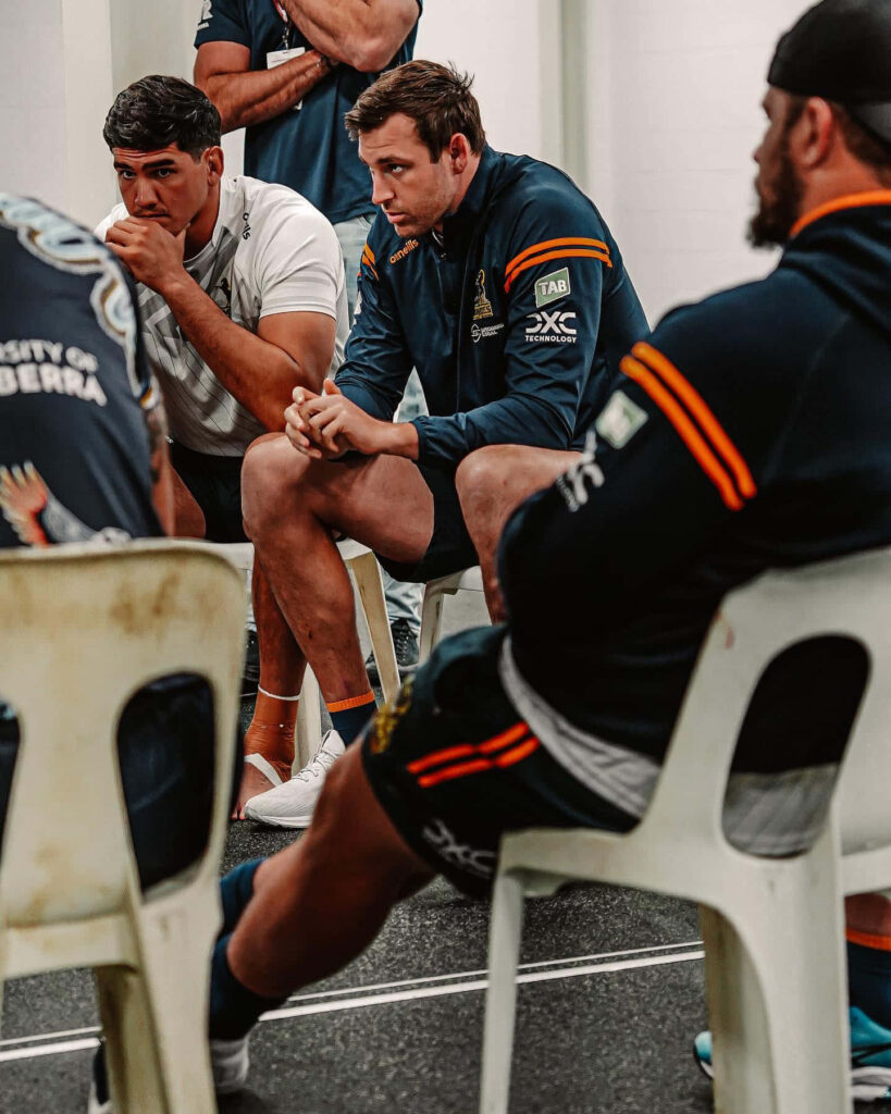 ACT Brumbies rugby players in navy gold uniforms deep in locker room team discussion wallpaper