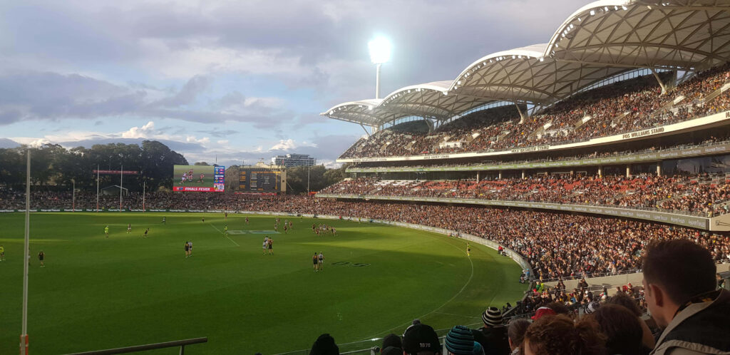 Adelaide Oval packed crowd watches exciting AFL match at dusk with dramatic skies and stadium lights Wallpaper