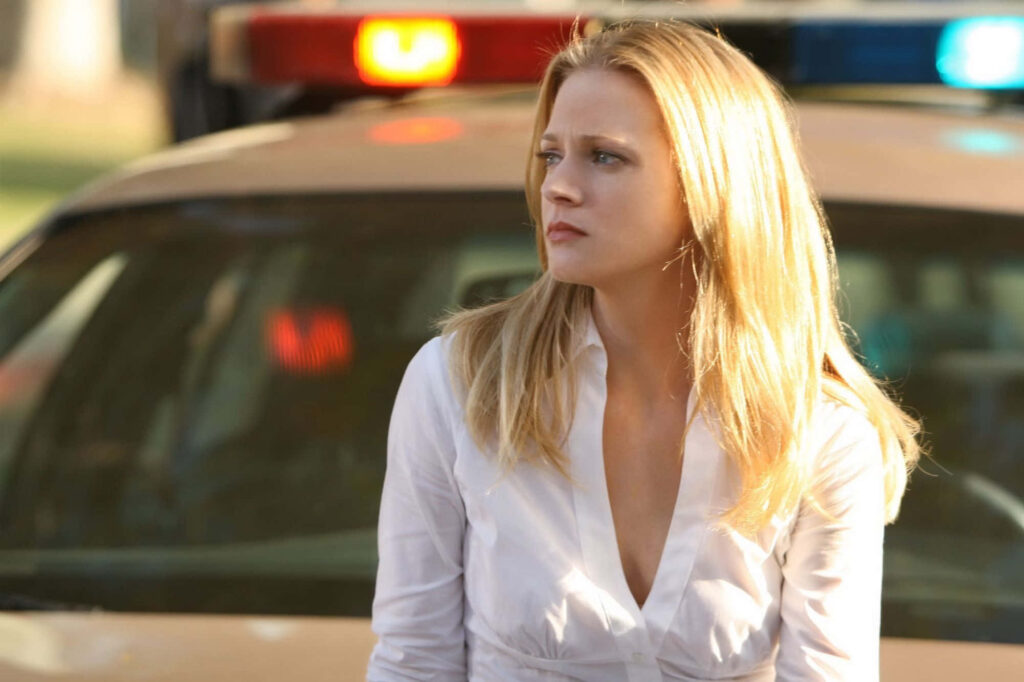 A J Cook confident and focused standing by police car with blonde hair in natural light background Wallpaper