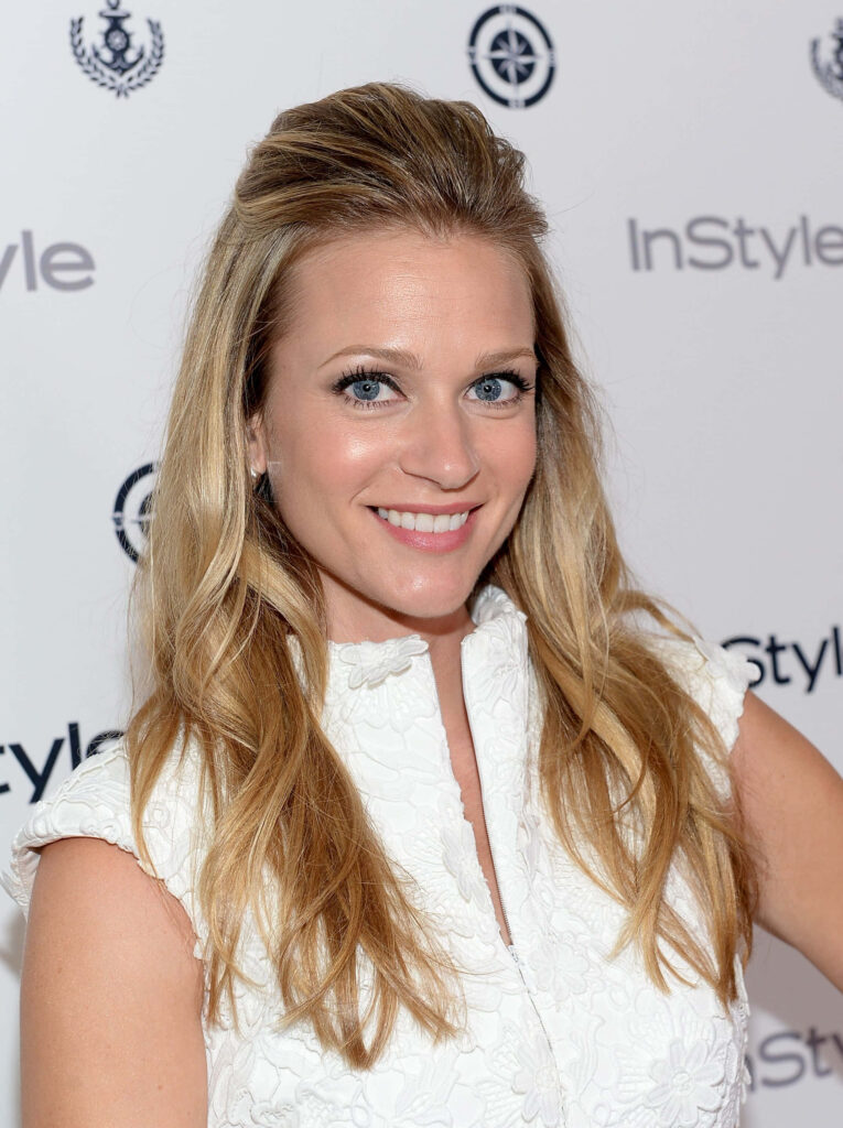 A.J. Cook smiling brightly with flowing blonde hair in elegant attire at stylish event backdrop Wallpaper
