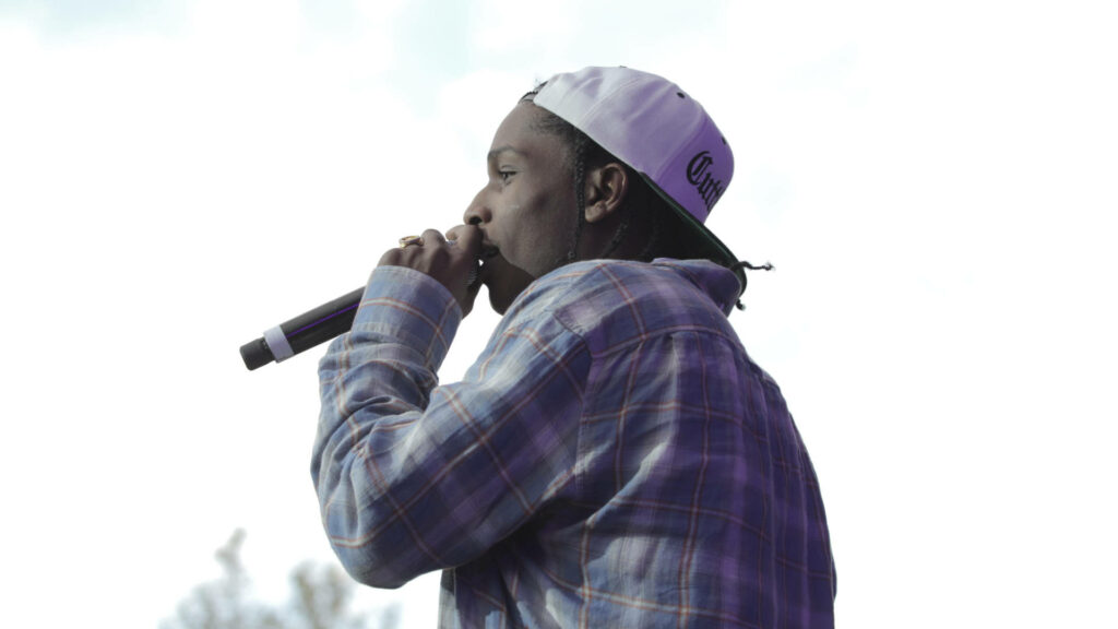 A$AP Rocky performing live in plaid shirt and white cap holding microphone against bright sky Wallpaper