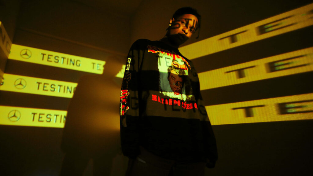 A$AP Rocky in dim room with yellow Testing and Mercedes-Benz projections on face and clothes Wallpaper