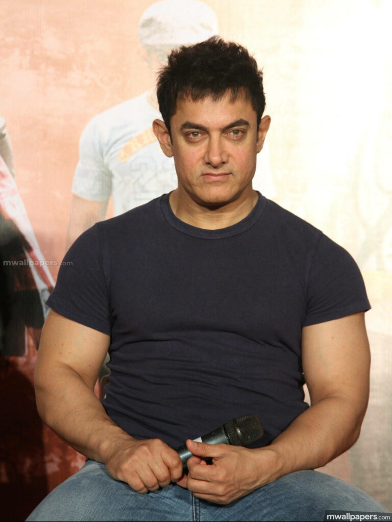 Aamir Khan speaking at movie press conference wearing navy blue t-shirt holding microphone focused Wallpaper