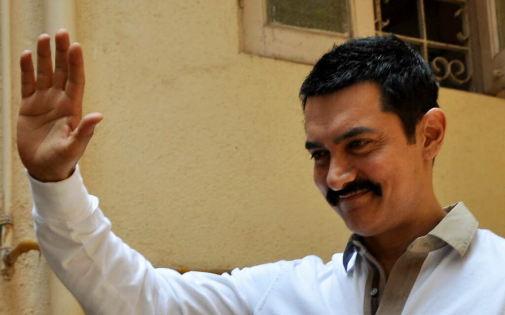 Aamir Khan smiling warmly and waving against a wallpaper background friendly charming actor