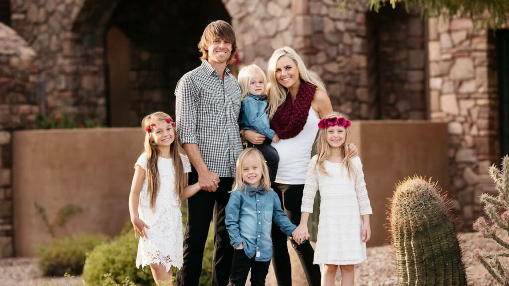 Aaron Baddeley and family smiling outdoors with rustic stone walls and desert plants background Wallpaper