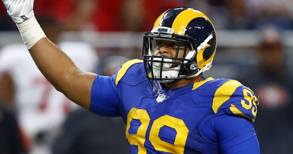 Aaron Donald Los Angeles Rams raising right hand in blue and yellow uniform on football field Wallpaper