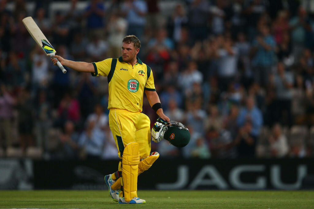 Aaron Finch celebrating with bat on cricket field wearing Australian yellow kit cheering crowd Wallpaper