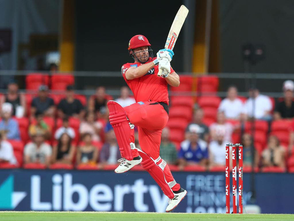 Aaron Finch in red cricket uniform playing a powerful shot on field with wallpaper background