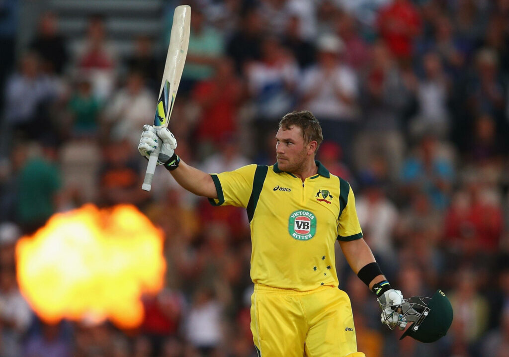 Aaron Finch in Victoria Bitter cricket uniform celebrating with raised bat and cheering fans Wallpaper