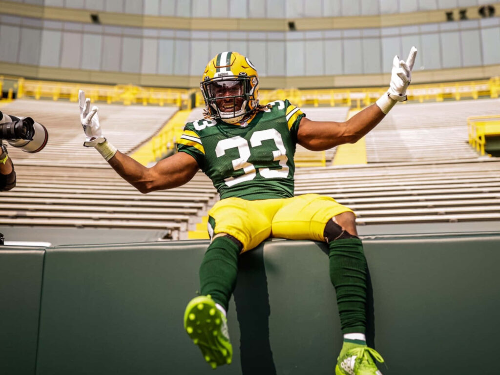 Aaron Jones Green Bay Packers NFL running back celebrates with arms raised game day energy stadium seats Wallpaper