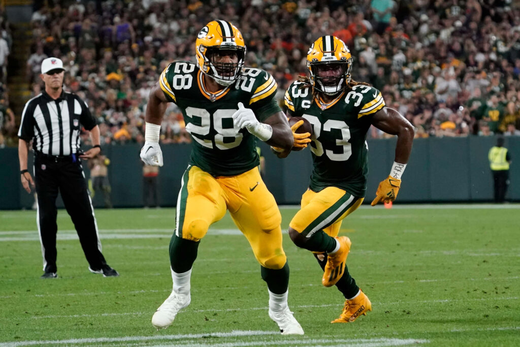Aaron Jones running with the football in Green Bay Packers uniform on game day field background Wallpaper