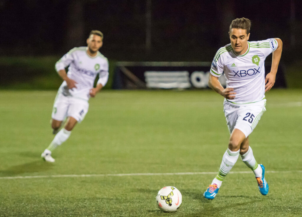 American soccer player Aaron Long in white and green kit moving ball forward 2015 match Wallpaper