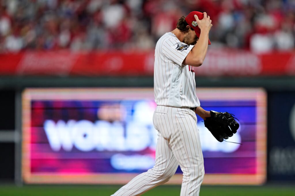 Aaron Nola in pinstriped uniform grips cap on field with focused crowd and World Series signage Wallpaper