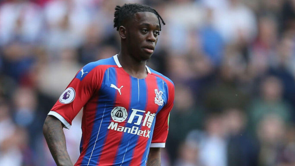Aaron Wan-Bissaka focused in Crystal Palace kit during intense match day with vibrant crowd background Wallpaper