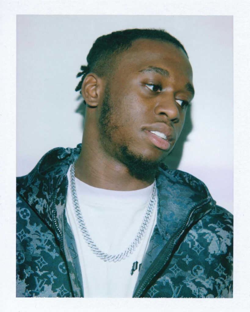 Aaron Wan-Bissaka stylish photoshoot wearing patterned jacket silver chain soft wallpaper background