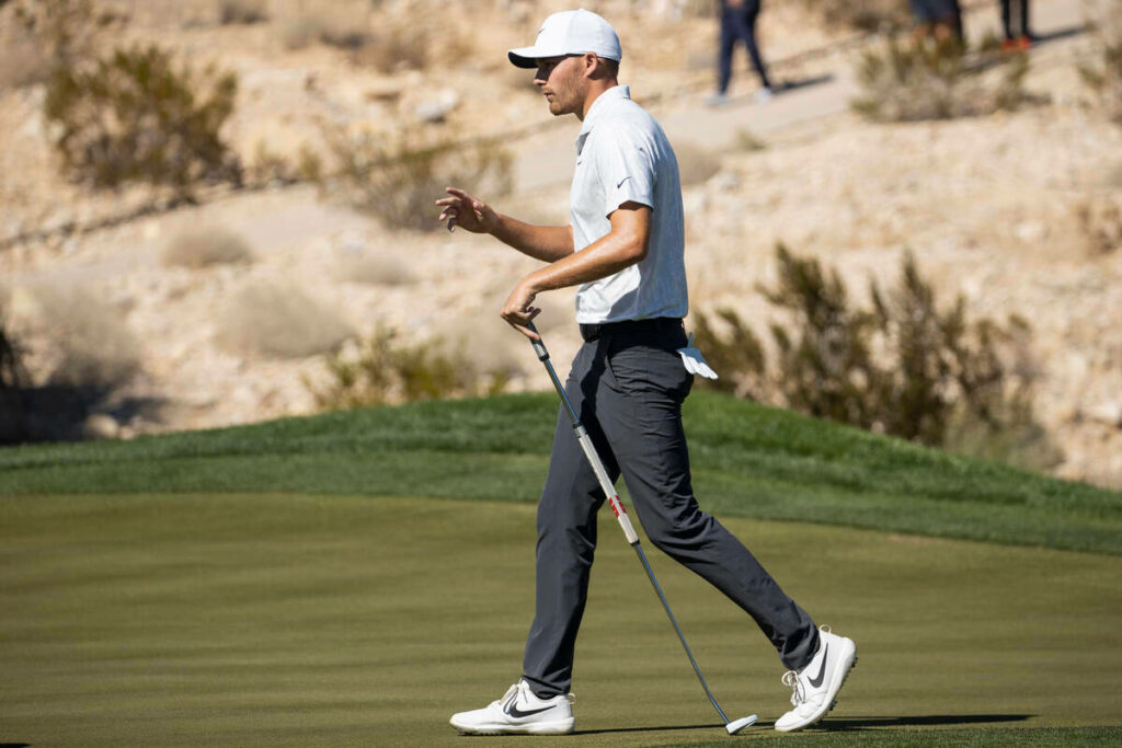 Aaron Wise walking confidently on golf course in white polo and cap with desert landscape background Wallpaper