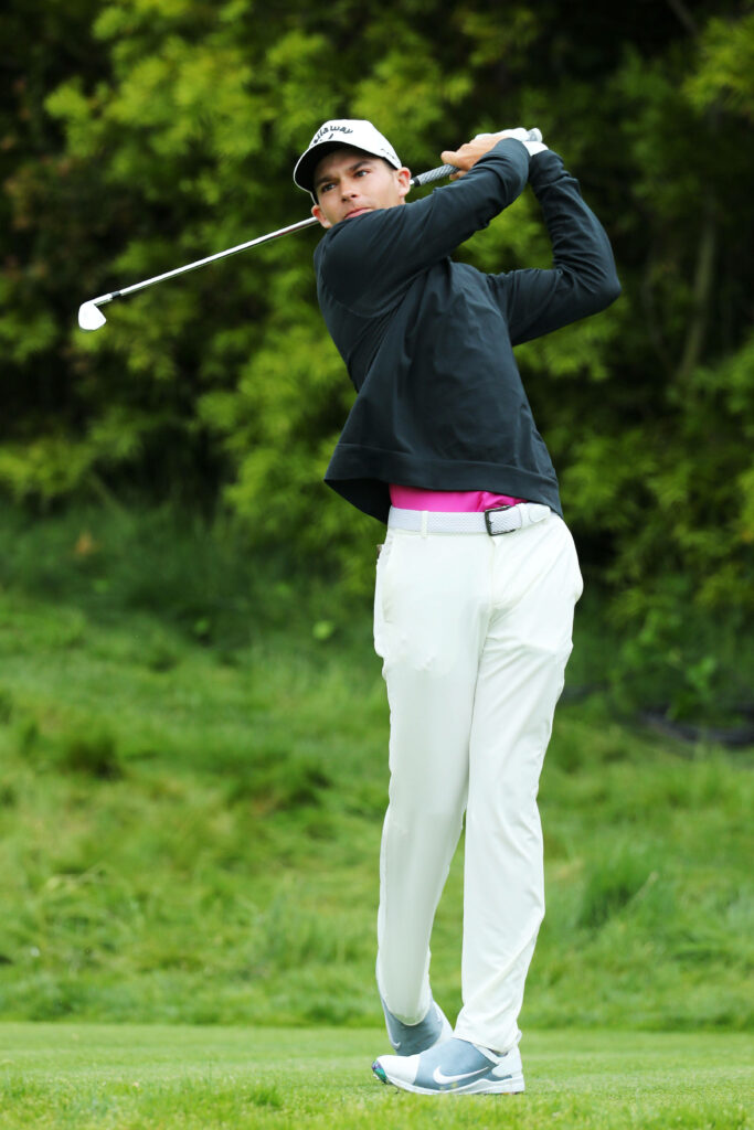 Aaron Wise mid-swing on lush green golf course with vibrant foliage and focused athletic form Wallpaper
