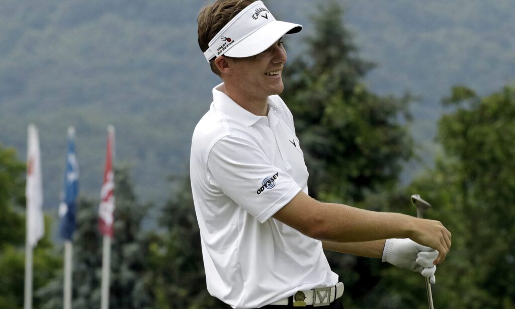 Aaron Wise smiling on golf course wearing white with lush trees and mountain scenic background Wallpaper