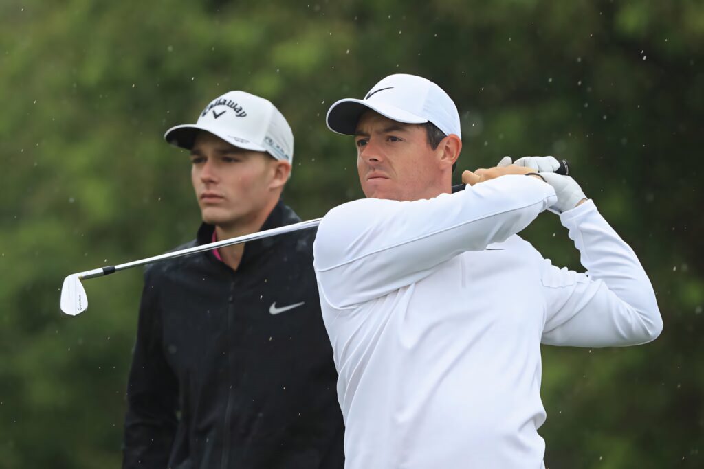 Aaron Wise and Rory McIlroy focused on golf course in sportswear against lush green backdrop wallpaper