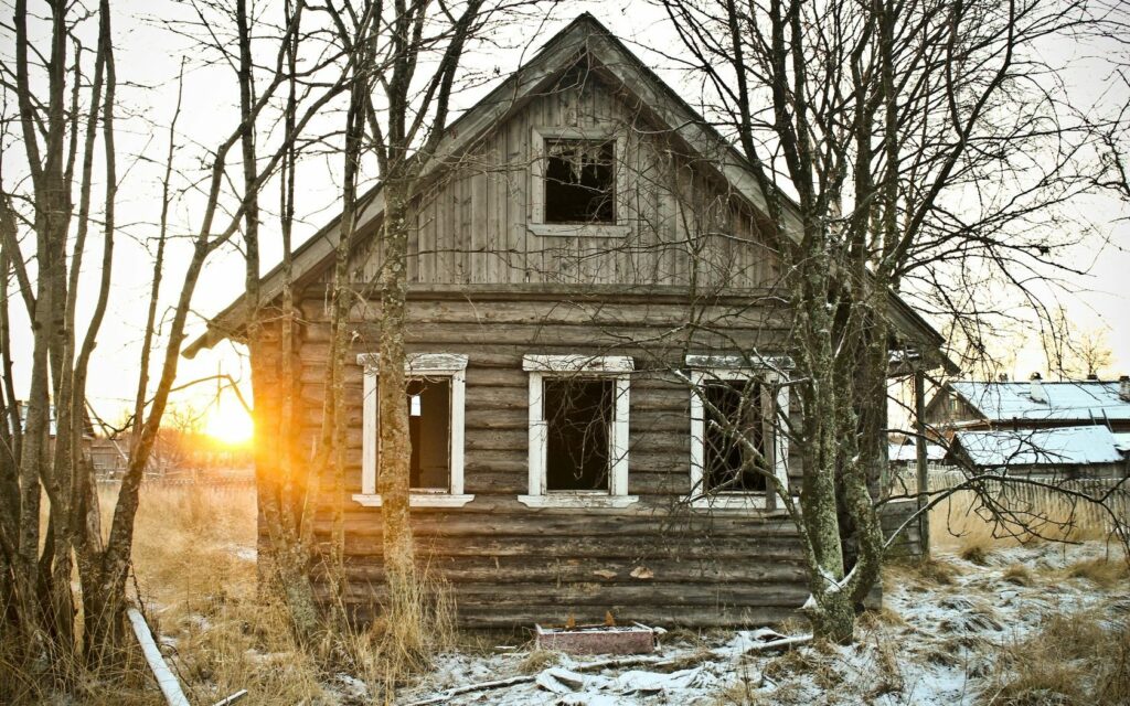 Abandoned log hut at autumn sunset surrounded by bare trees and frosty grass wallpaper background