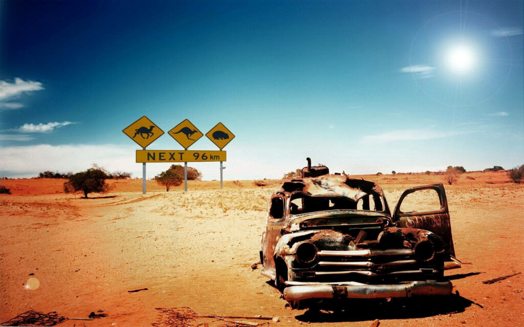 Rusted old car abandoned under sun in Australian Outback near wildlife warning road signs wallpaper