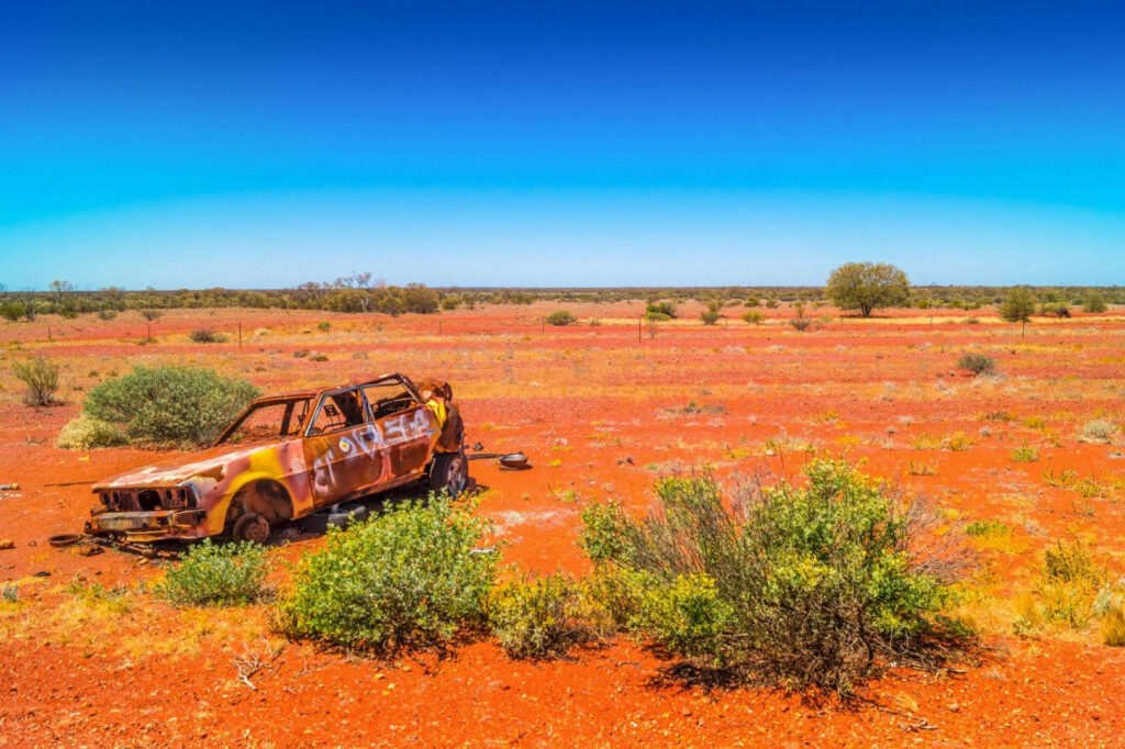 Abandoned rusted car in red sand and shrubbery of Australian Outback under clear blue sky wallpaper