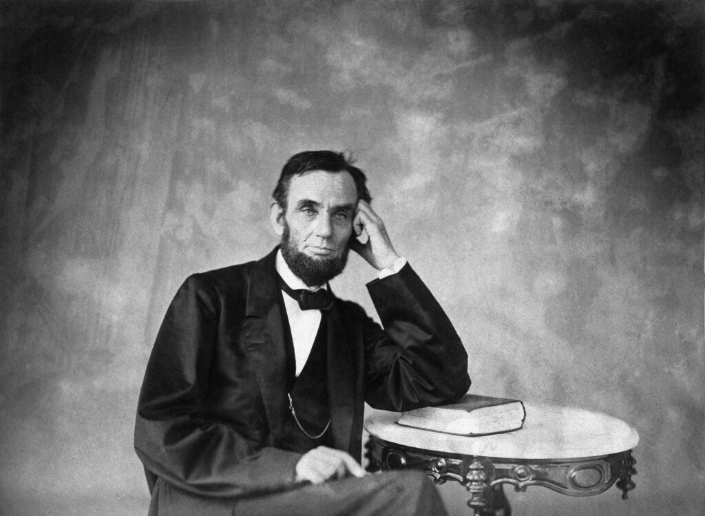 Classic half body Abraham Lincoln portrait seated at table with open book soft textured background Wallpaper