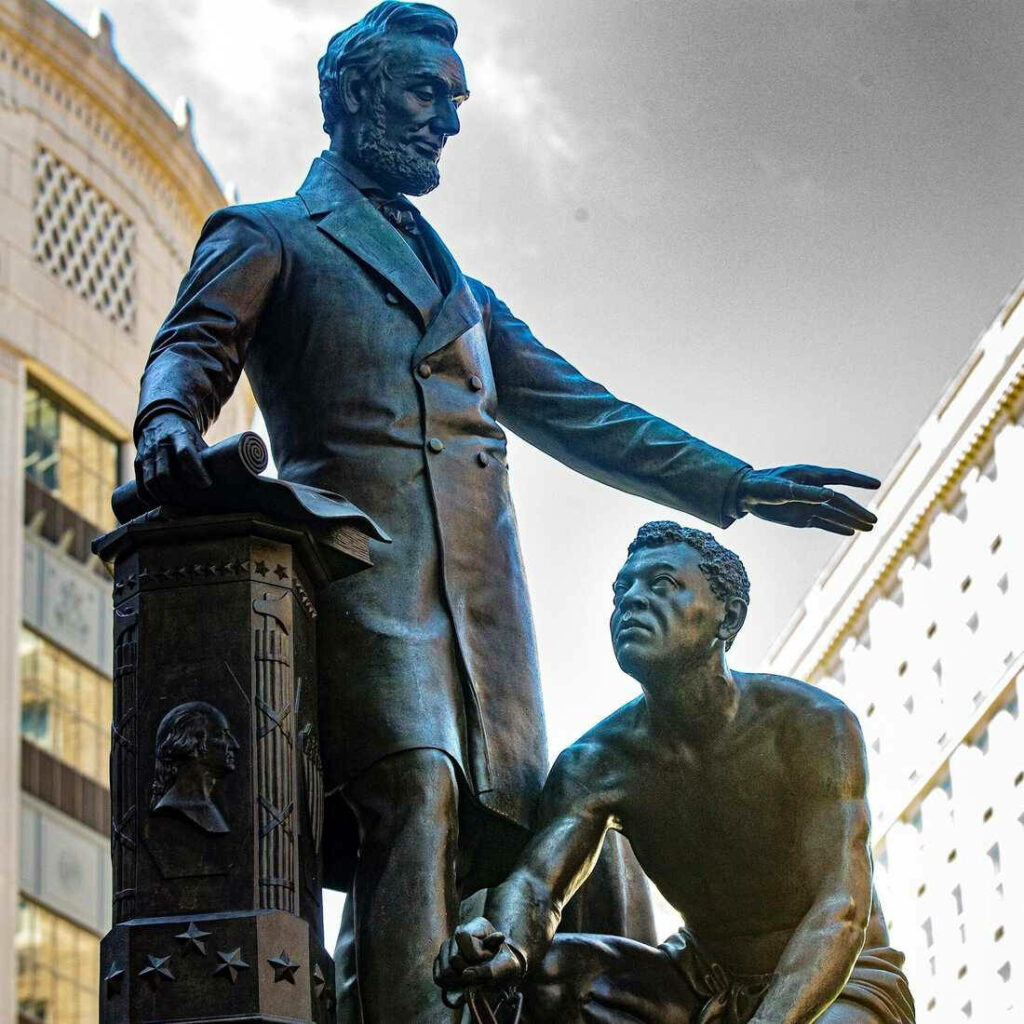 Bronze Statue of Abraham Lincoln with freed slave symbolizing emancipation against cityscape Wallpaper