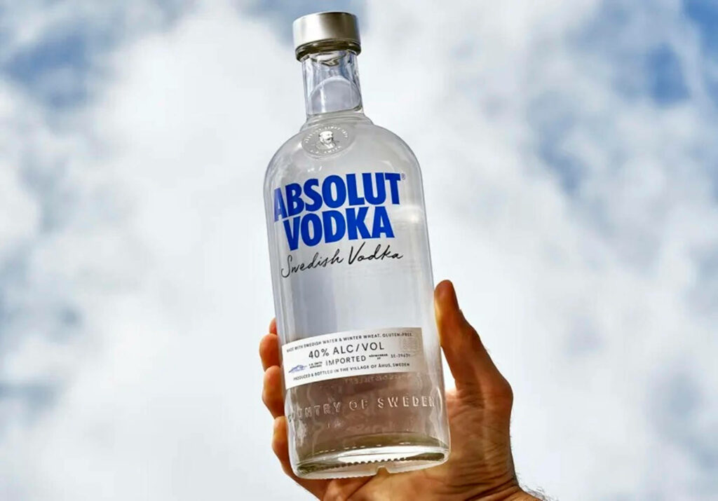 Clear Absolut Vodka bottle held against bright sky showcasing Swedish origin and pure design Wallpaper