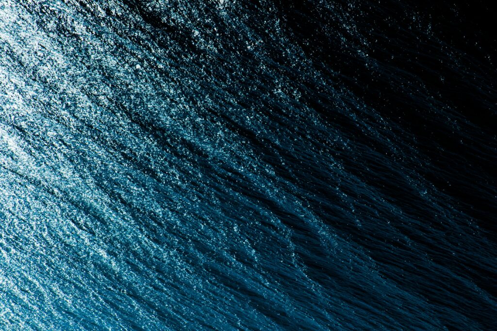 Abstract blue and black water surface with shimmering spray and reflective light wallpaper background