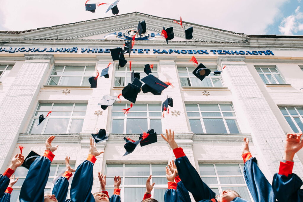 Fresh graduates in blue and red gowns toss caps near National University of Food Technologies Ukraine Wallpaper